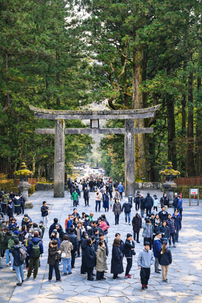 日光東照宮の石鳥居と参道を歩く参拝客、荘厳な世界遺産の風景