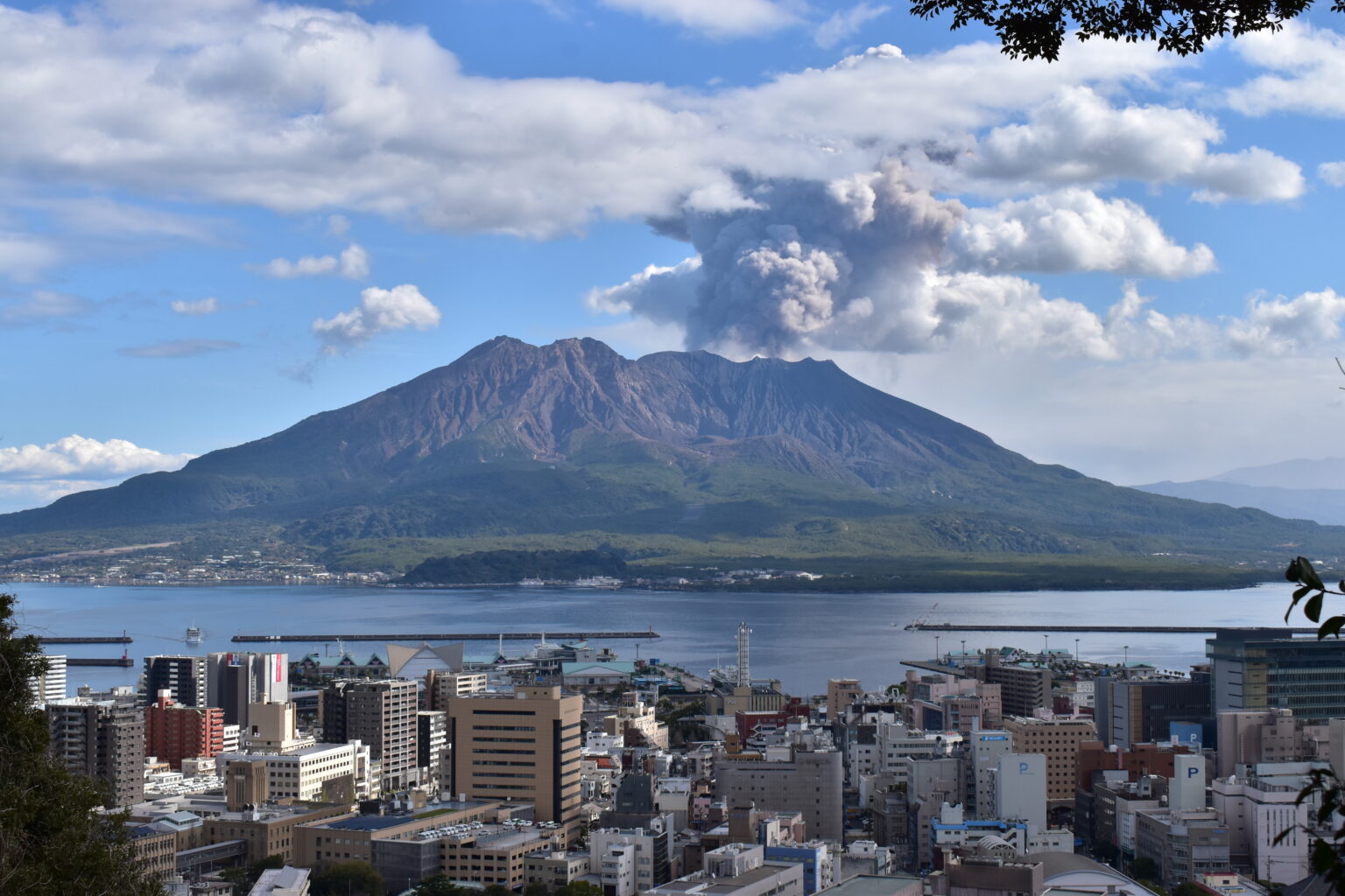 鹿児島市街地越しに見える噴煙を上げる桜島（Web面接で訛りを指摘された鹿児島出身27歳のイメージ）