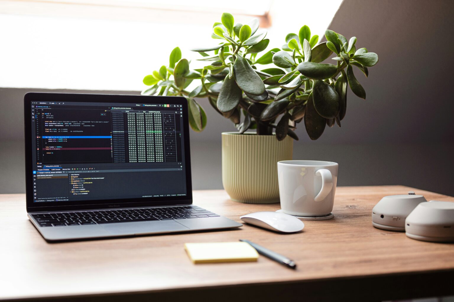 木製デスクに置かれたMacBookと観葉植物、コーヒーカップのある作業スペース